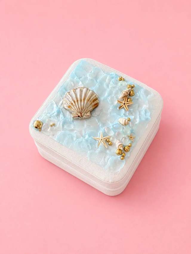 Weiße Reise-Schmuckbox mit selbst gestaltetem Resin-Deckel in Meeresoptik: blaue Wellen, echte Jakobsmuschel, Seesterne, Schneckenhäuser und Goldperlen